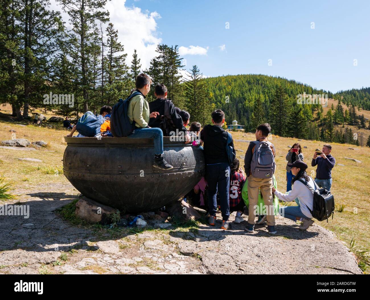 Children posing for photo in 18th century bronze cauldron used to cook food for pilgrims, Manzushir Khiid Monastery, Mongolia Stock Photo
