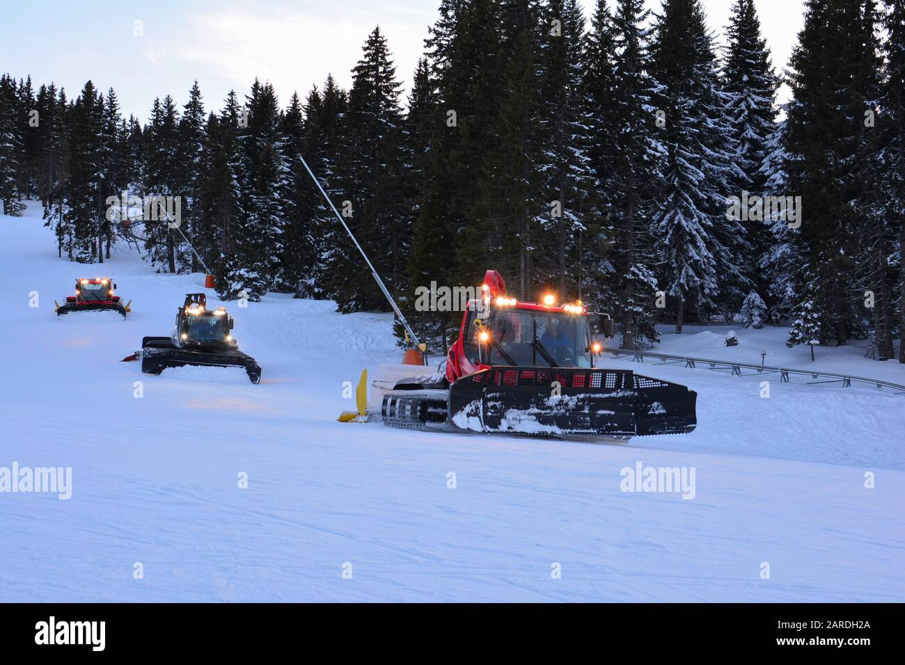 Three snowcat vehicles in line after sunset, in action of ski slope preparation for next day, ski resort Kopaonik, Serbia Stock Photo