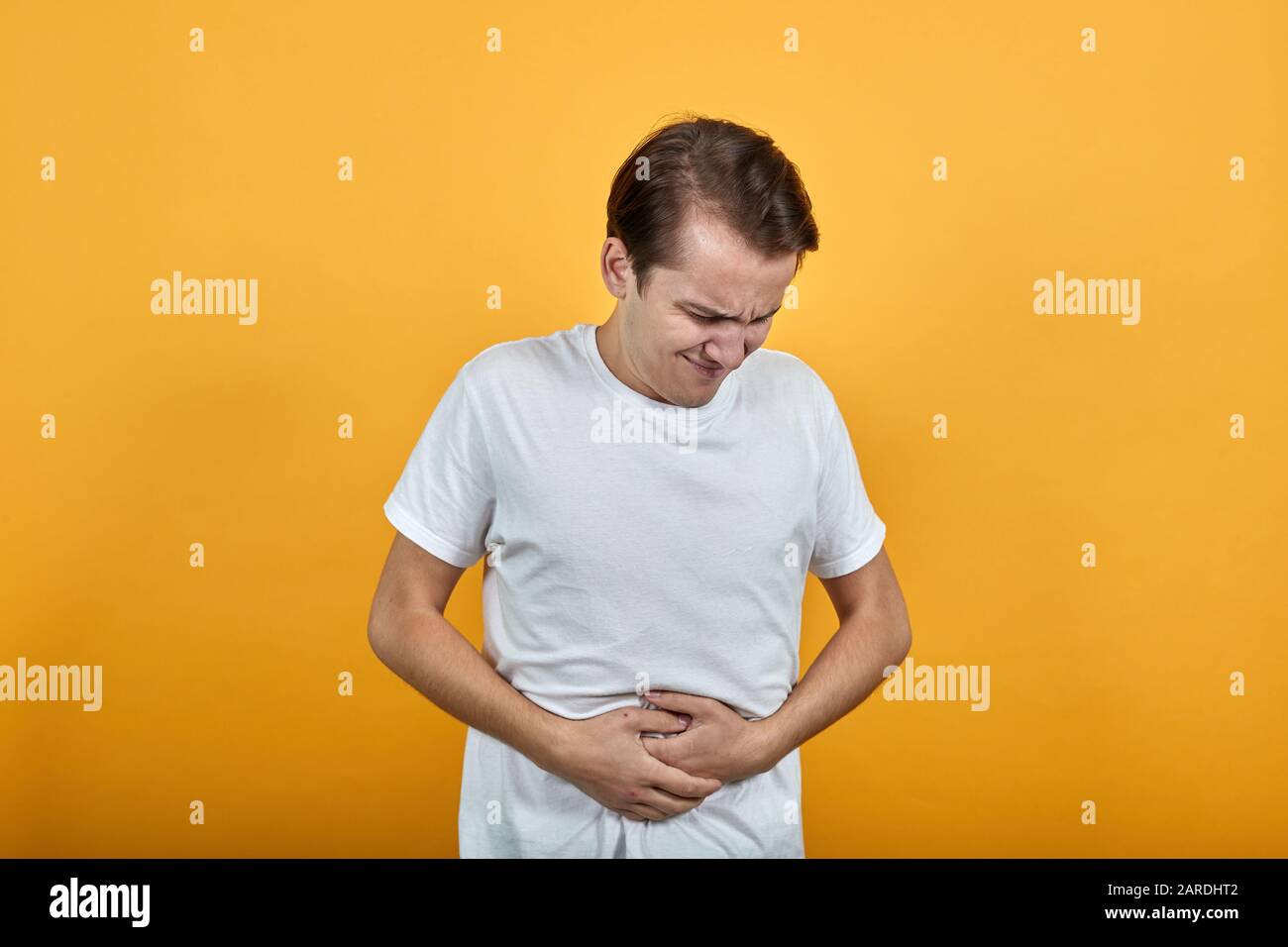 Stomach pains stomach problems white Tshirt young male on yellow