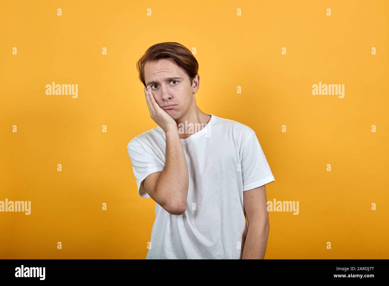 A perplexed man in white t-shirt looks ahead in confusion, leaning head ...