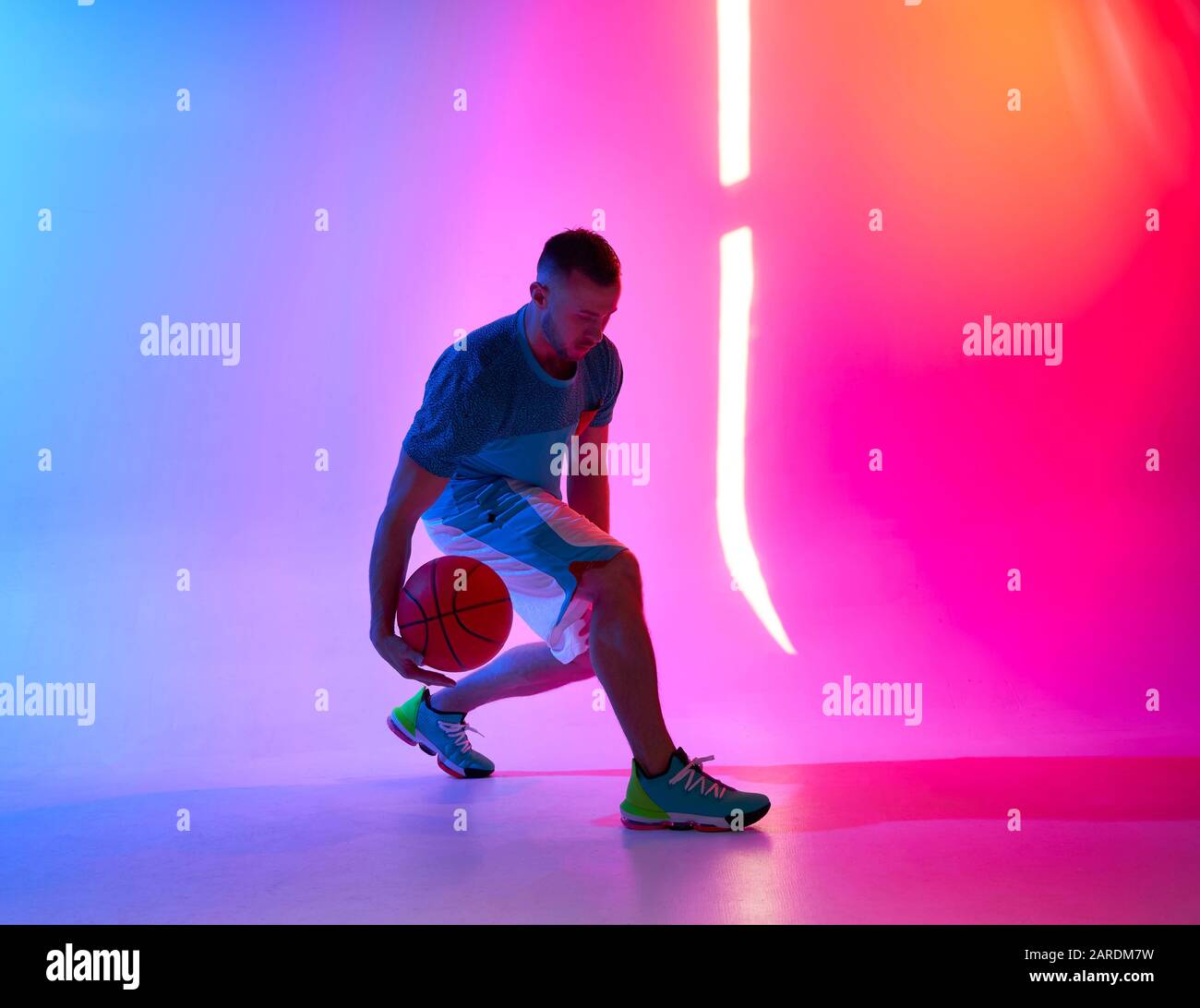 Young athletic man dribbling with basketball ball posing on mix of blue