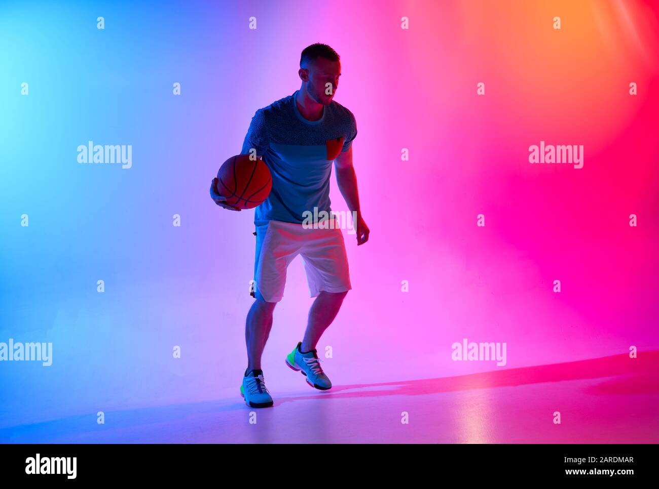Young athletic man dribbling with basketball ball posing on mix of blue