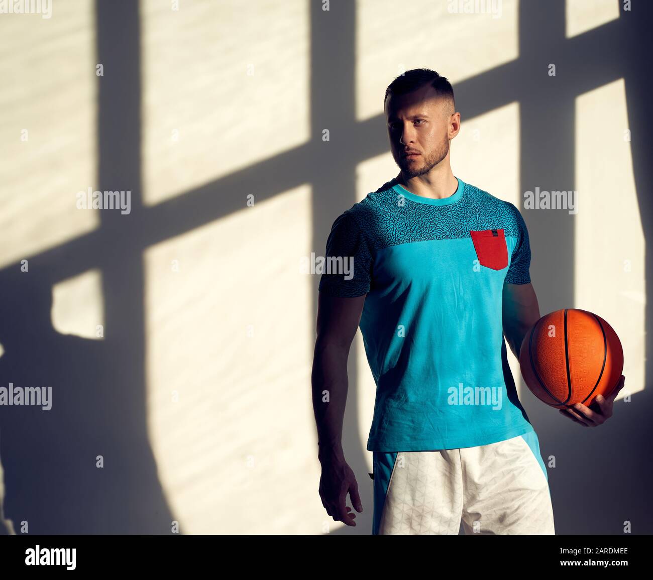 Young athletic man, basketball player holding ball and standing near