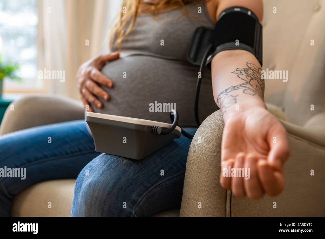A closeup shot on the tattooed arm of a young pregnant woman using a digital sphygmomanometer to measure blood pressure at the brachial artery Stock Photo