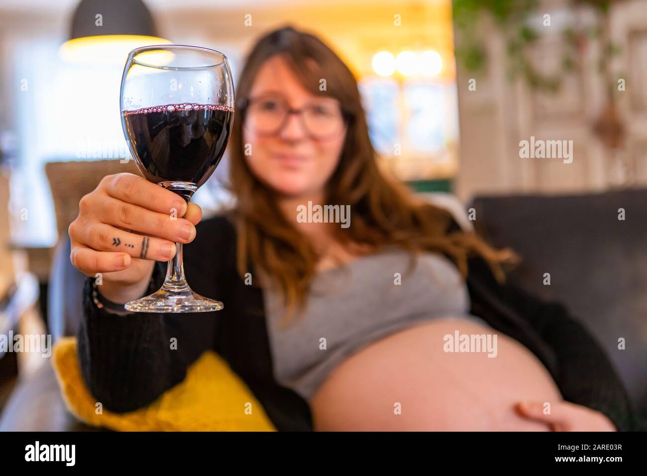 A selective focus view of a pregnant woman in third trimester enjoying a glass of red wine at home, risking health of unborn baby, copy space to right Stock Photo