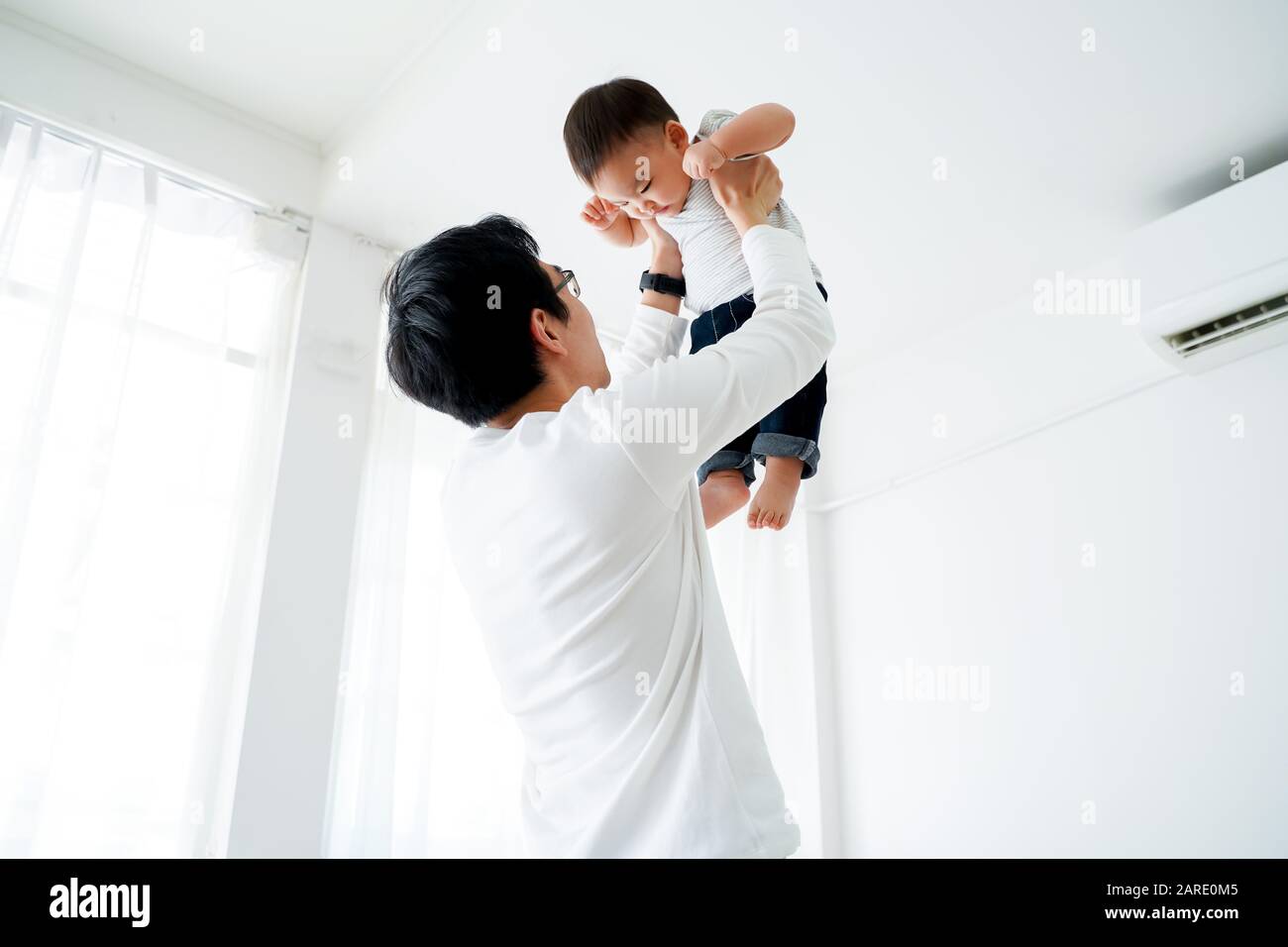 Young adult 30s Asian father lifting his little own son up flying in the air in bedroom at home. Family time and fatherhood concept in Asia Stock Photo