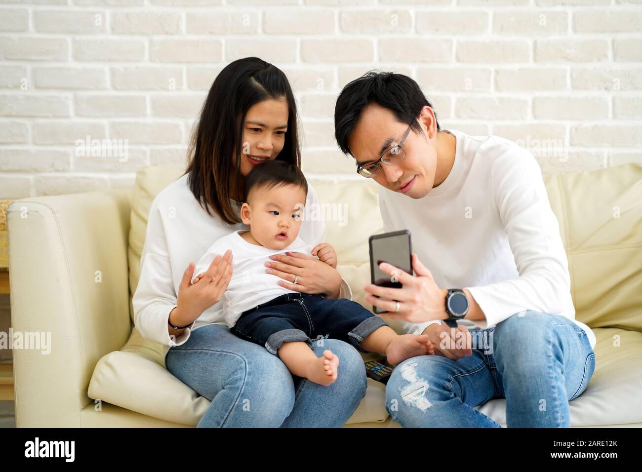 Cheerful Young Asian Family With Son Watching Video On Mobile Phone And Sitting On Sofa Couch At Home Parents And Kid Enjoying Cartoon Movie Stock Photo Alamy