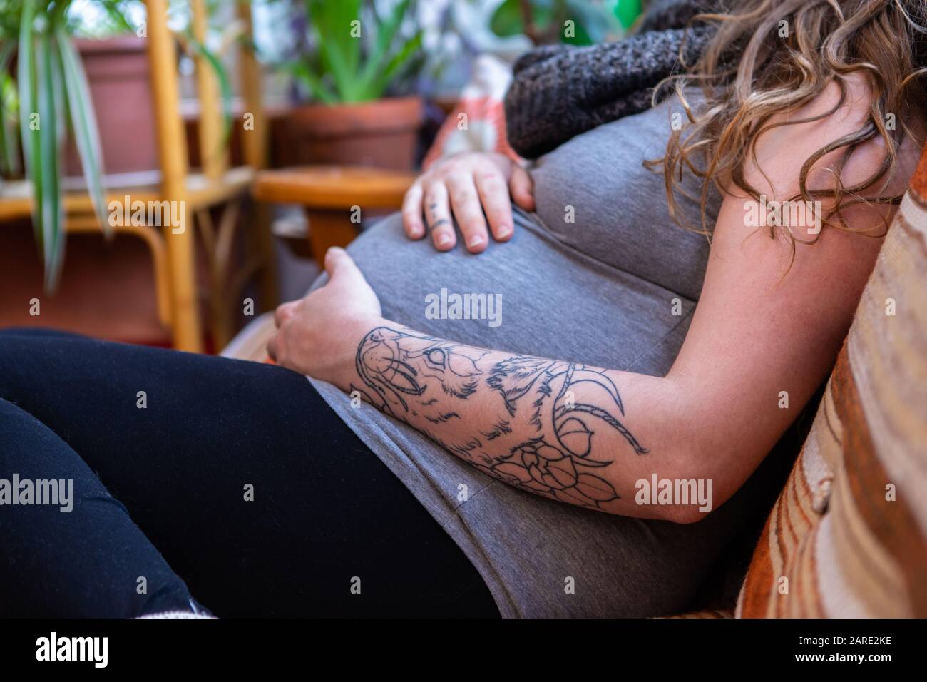 A close up shot of a heavily pregnant woman in the third trimester relaxing on sofa in family room, feeling movements and kicks with hands near labor Stock Photo