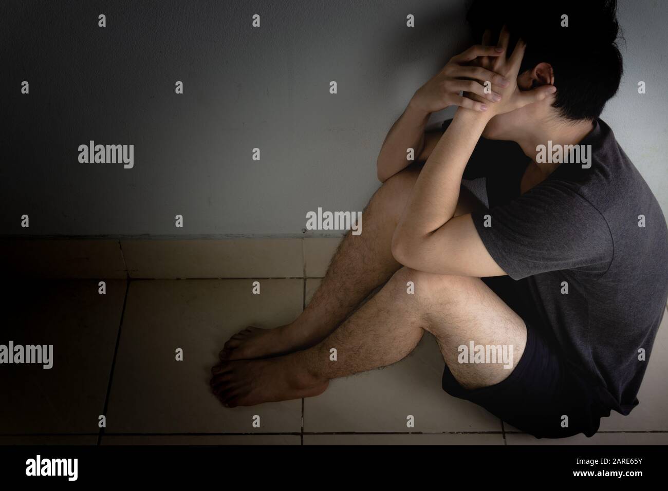 sad man hug his knee and cry sitting alone in a dark room. Depression ...