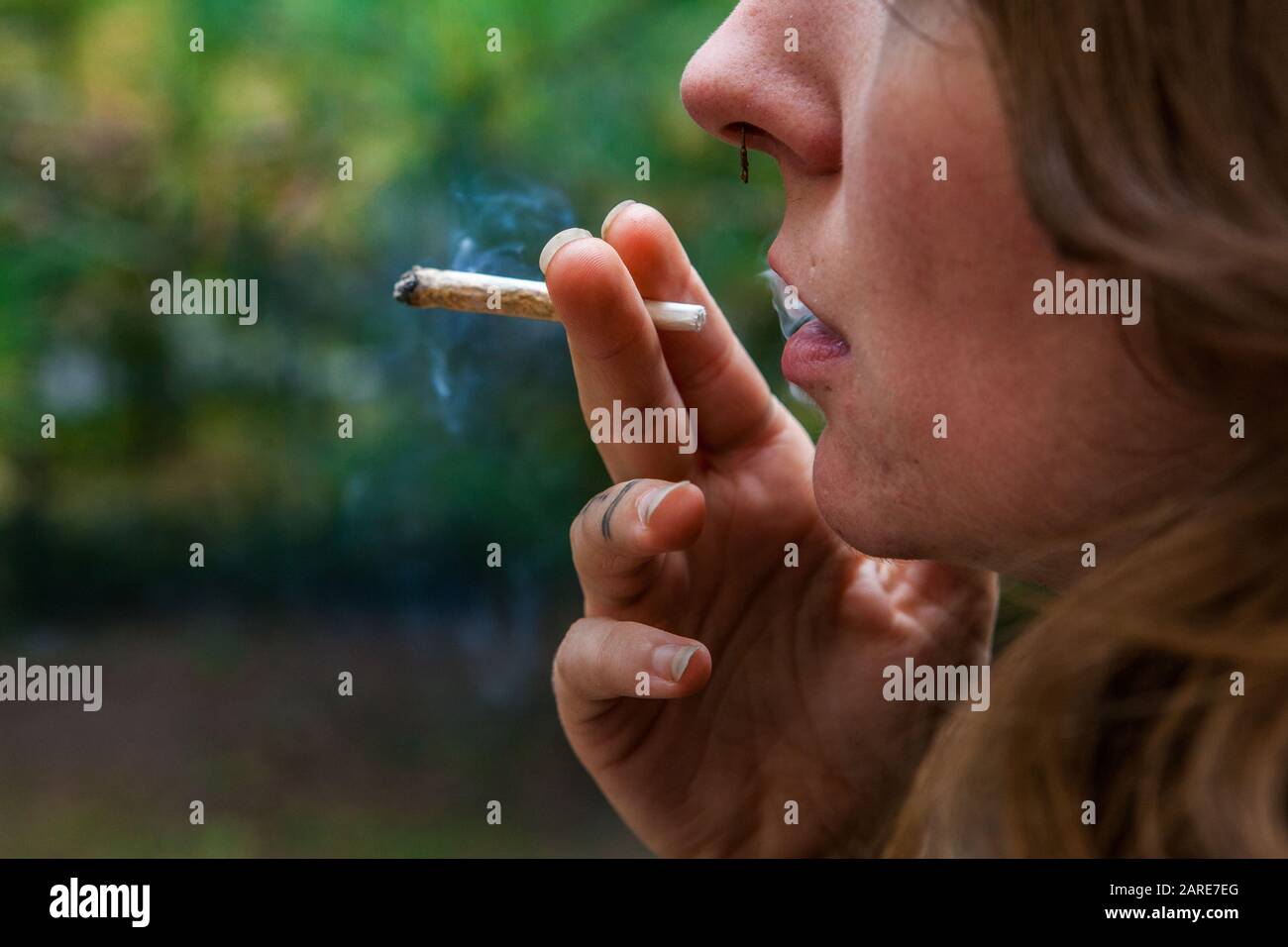 Closeup shot of lower half of caucasian woman's face smoking hand rolled marijuana joint. the freshly lit cannabis cigarette held between her two fingers.  Stock Photo