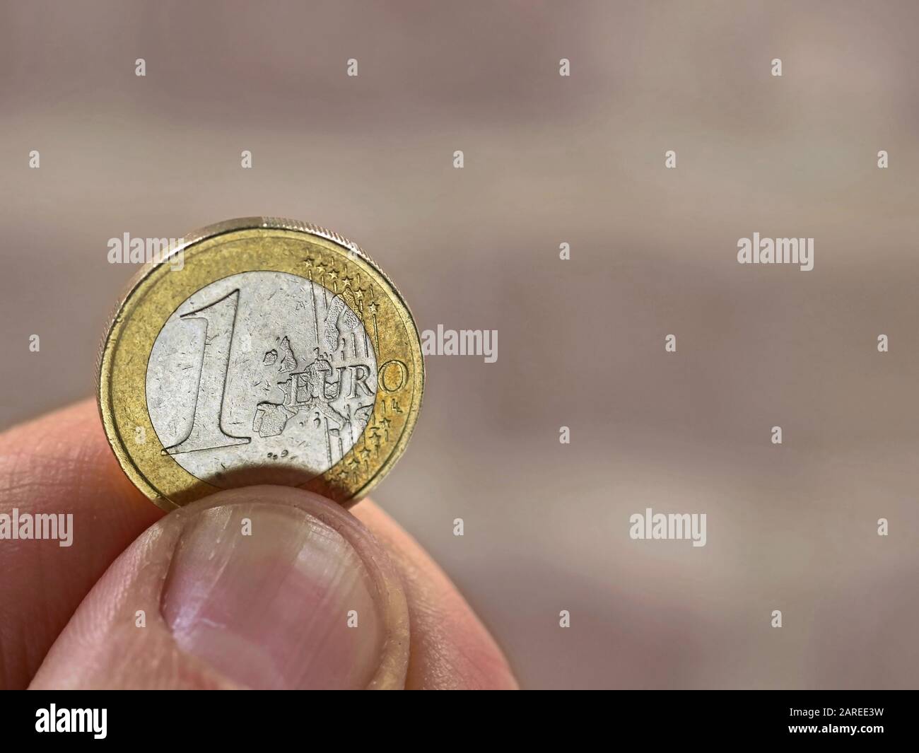 male hand holding a one euro coin on blurred background with copy space Stock Photo
