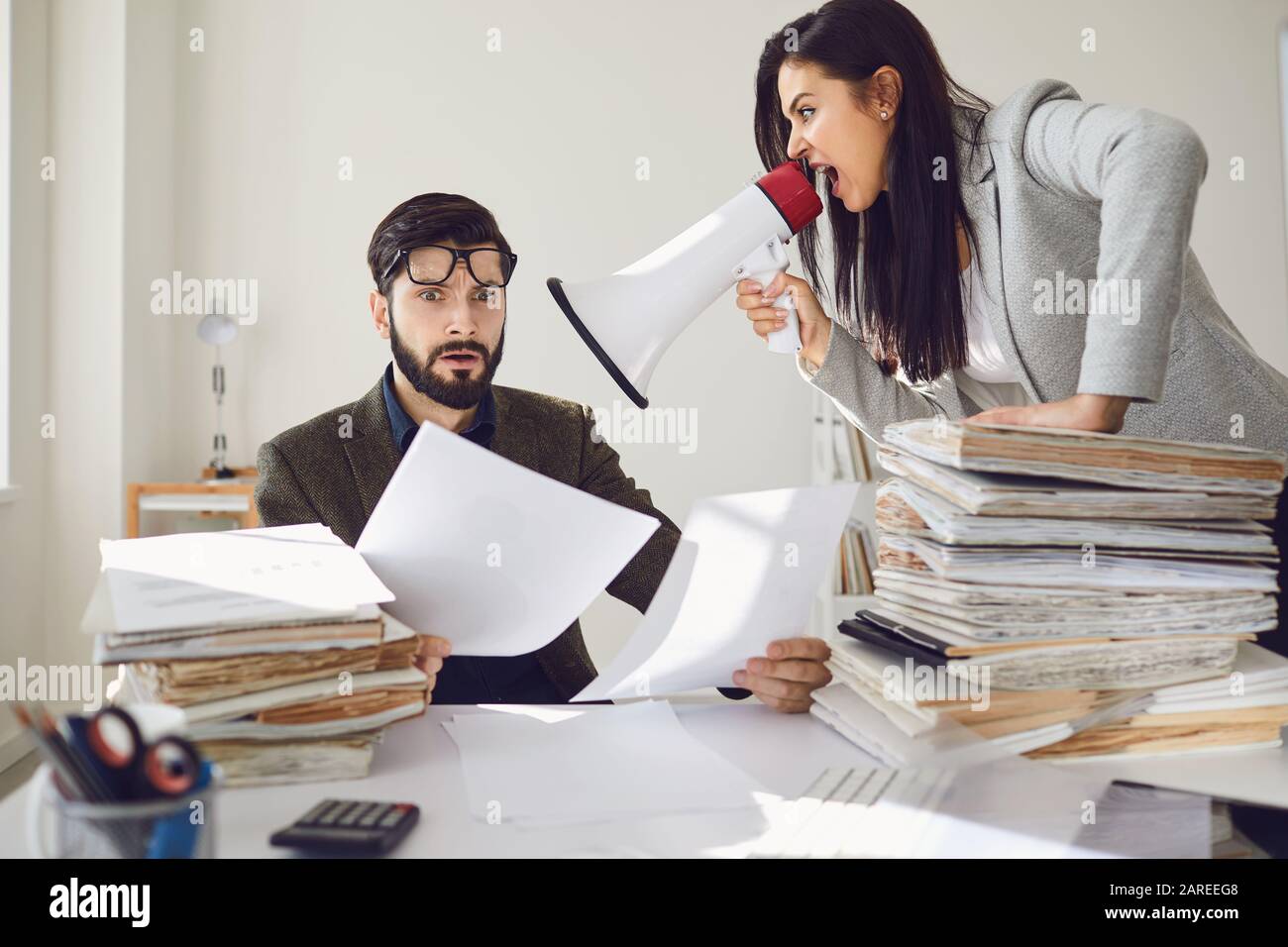 Angry boss businesswoman shouting at her office worker in a megaphone in the office Stock Photo