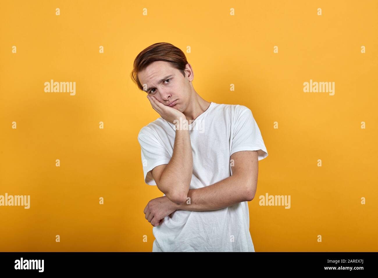 handsome man in white t-shirt looks distressed at camera with head on hand Stock Photo