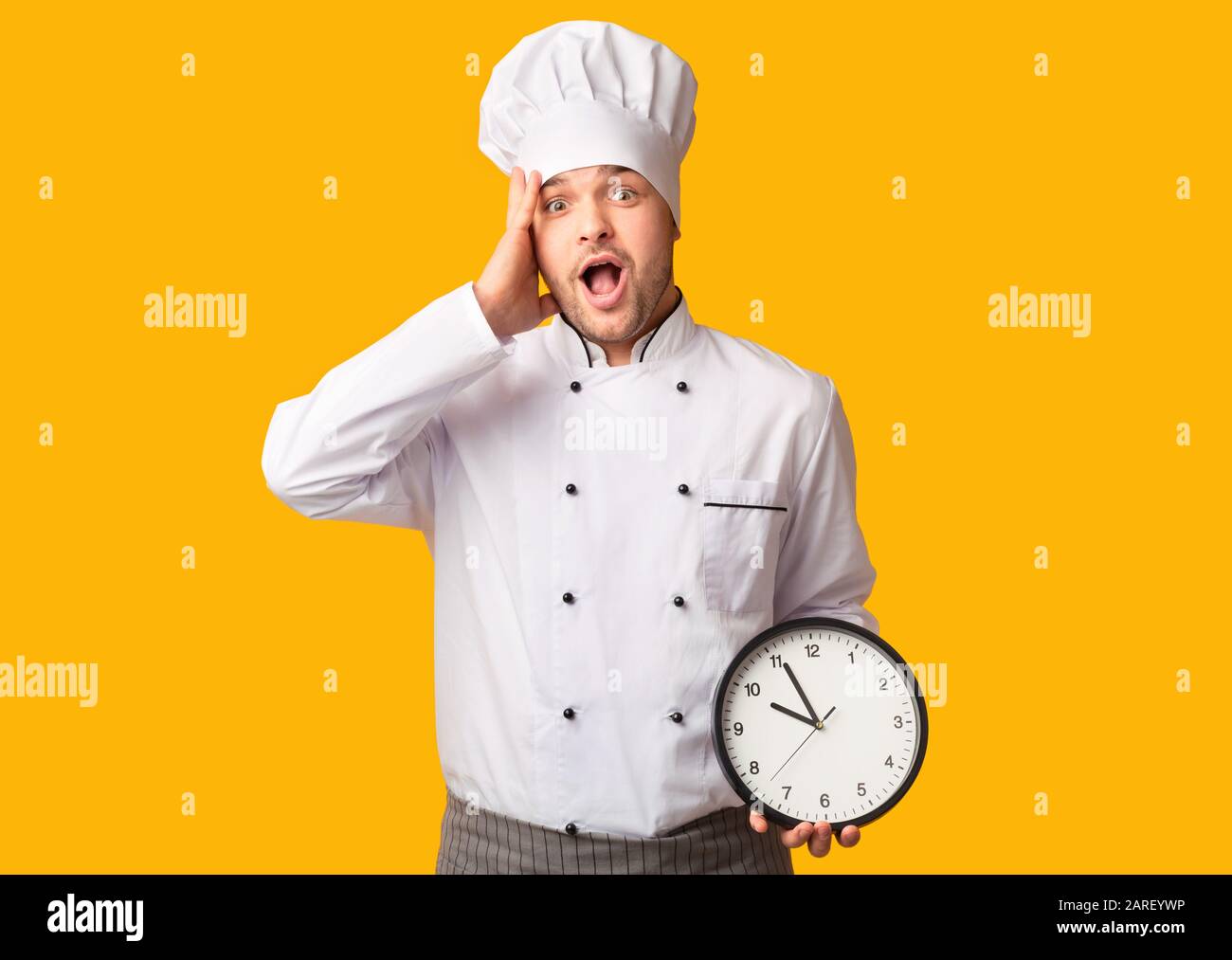 Shocked Cook Guy In A Hurry Holding Clock, Studio Shot Stock Photo