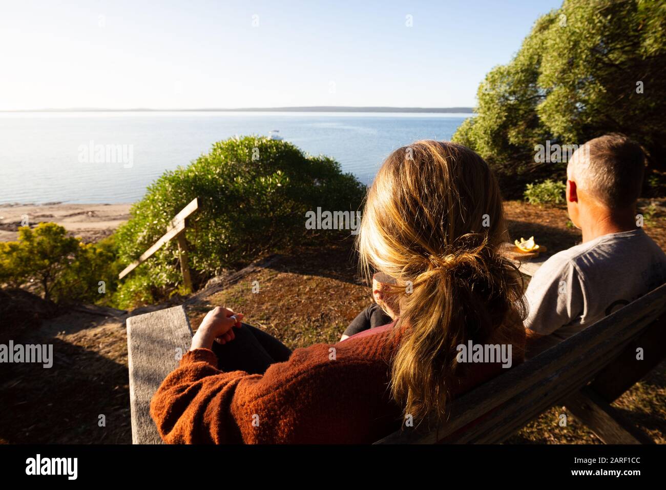 Mature couple sitting in front yard of home with beautiful bright morning view of beach and sea in Australia. Stock Photo
