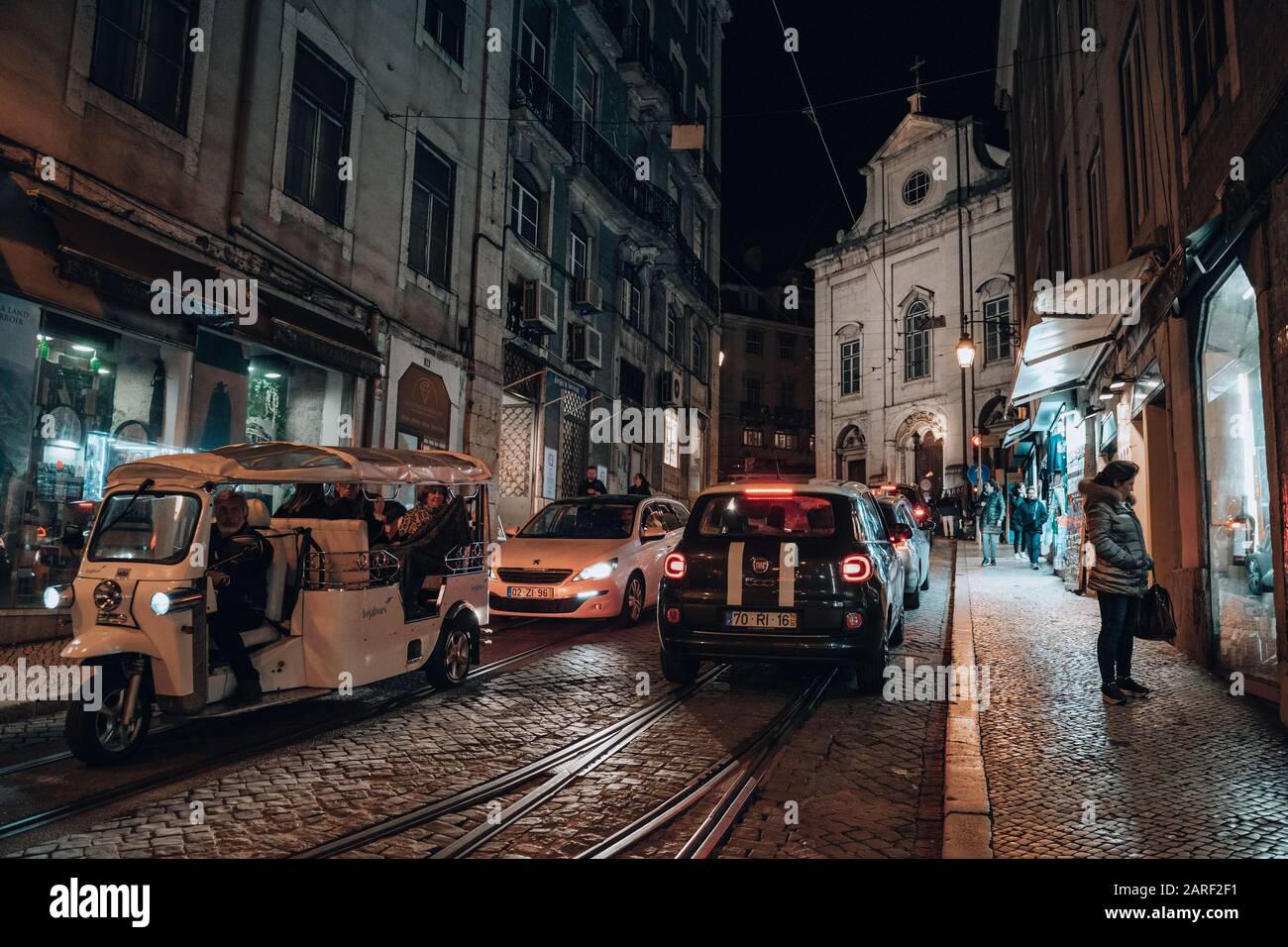 Lisbon, Portugal - January 19, 2020: Night street view of Lisbon, with cars and tuk tuk on the streets lined with shops Stock Photo