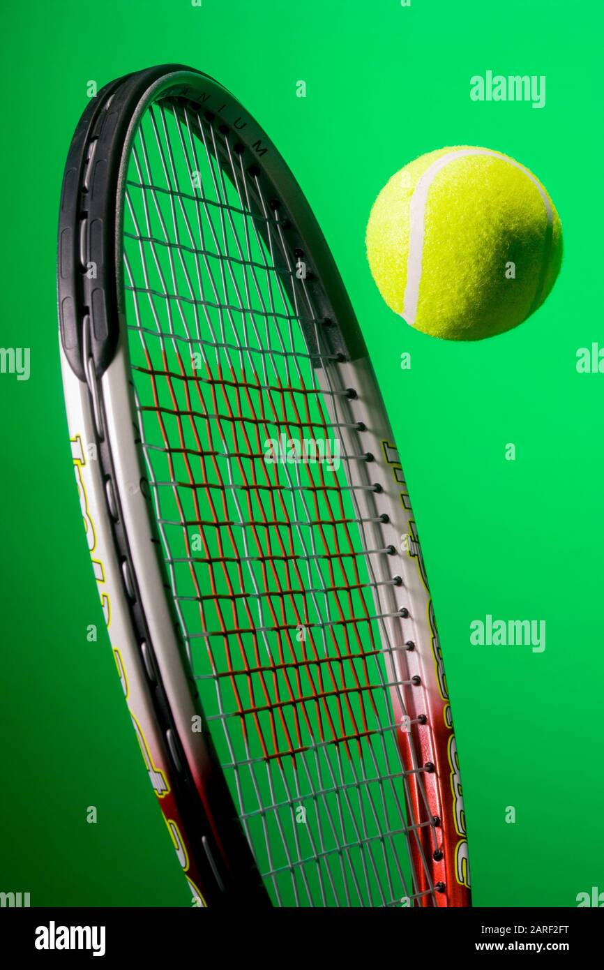 Tennis Racket with yellow tennis ball against green background Stock Photo