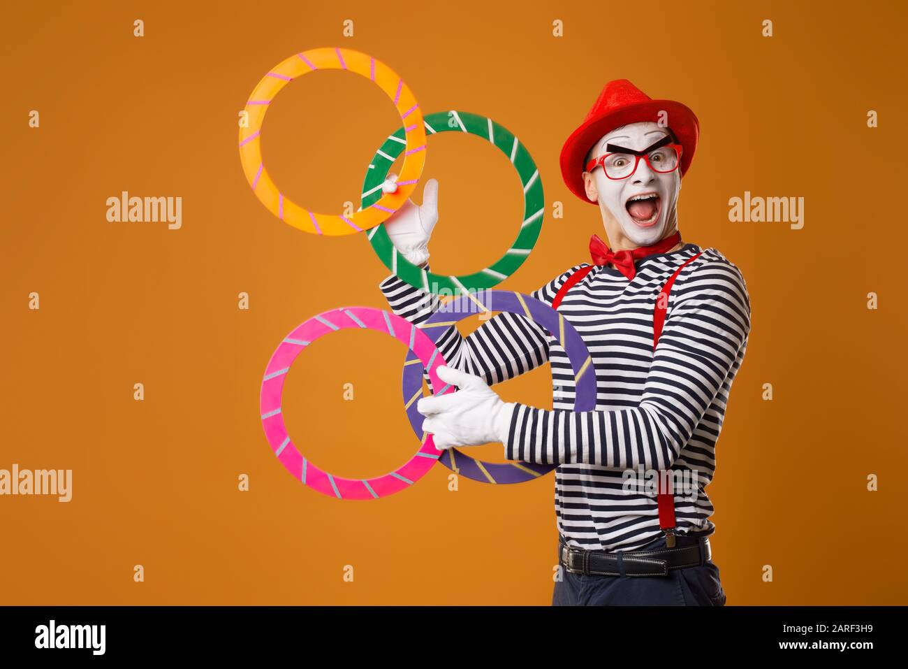 Happy mime with multi-colored rings on empty orange background Stock Photo