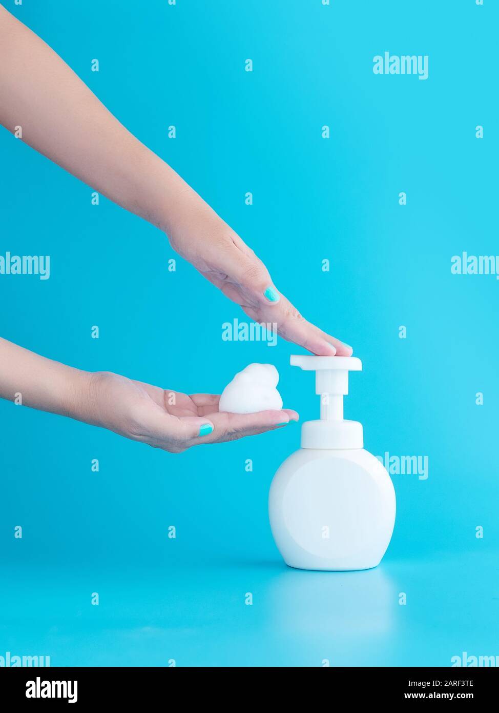 plastic pump bottle and mousse foam or cleansing foam on woman hand isolated on blue background, vertical with copy space. cleaning concept Stock Photo
