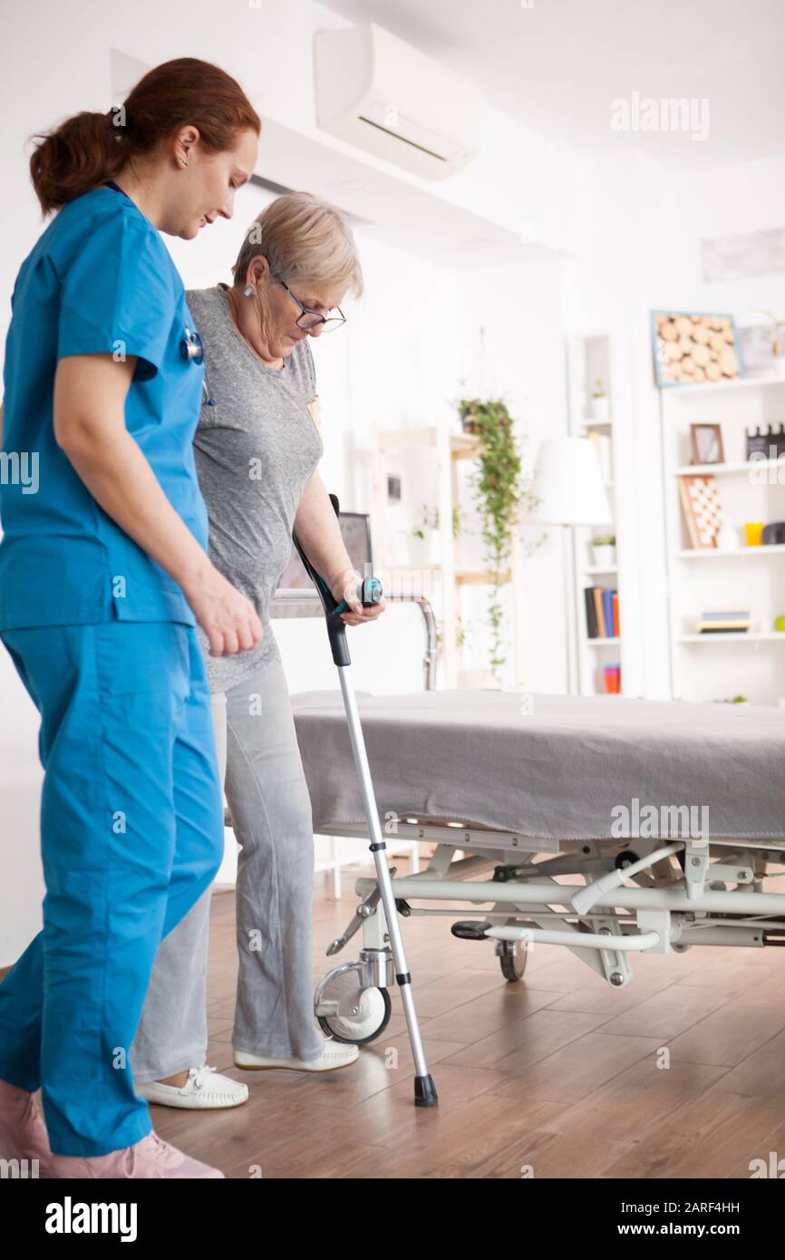 Female nurse helping old woman with walking problem in nursing home