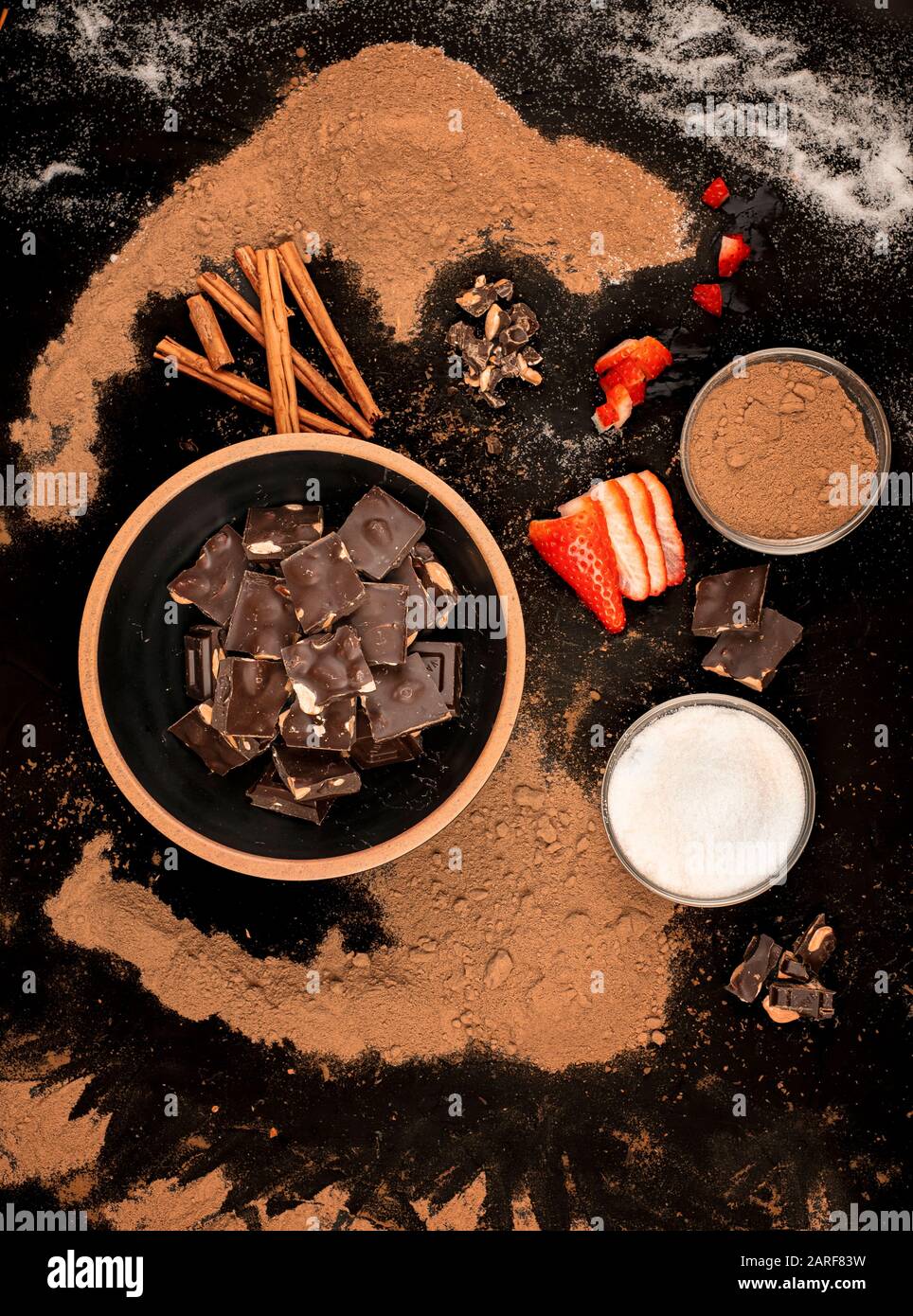 bowl of chocolate pieces bowl of sugar and cocoa with pieces of strawberries and cinnamon ,on a black background Stock Photo