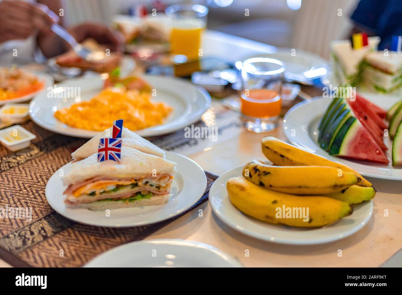 Healthy Breakfast Concept. Club Sandwich presented with English Flag on top along with fruits and juice at breakfast table. Stock Photo