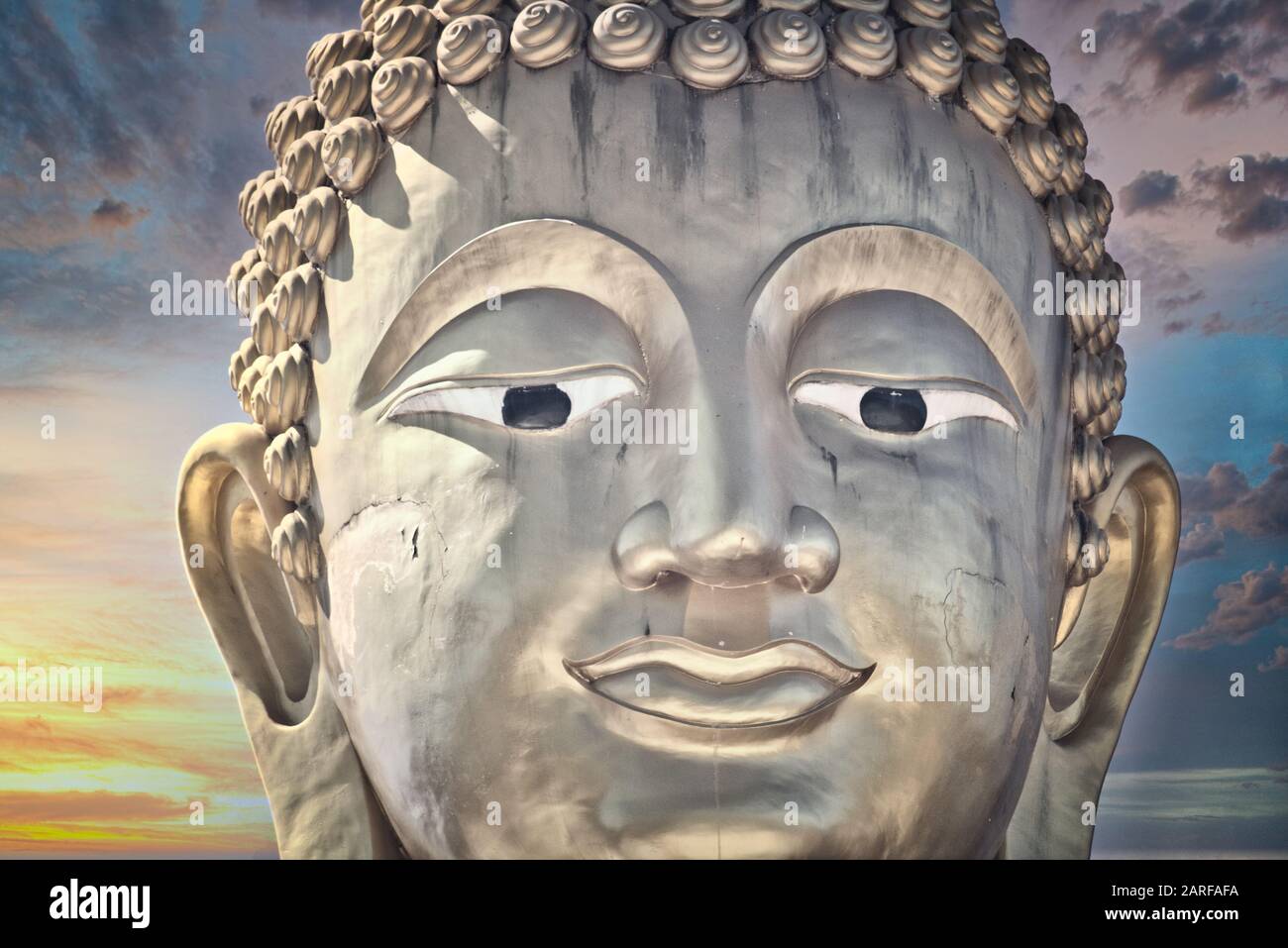 This unique photo shows the golden head of a large Buddha statue and a dreamy sunset with red clouds in the sky of Hua Hin in Thailand. Stock Photo