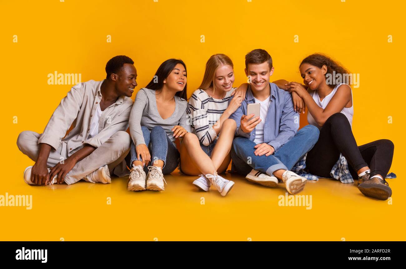 Relaxed students watching content on smartphone together Stock Photo