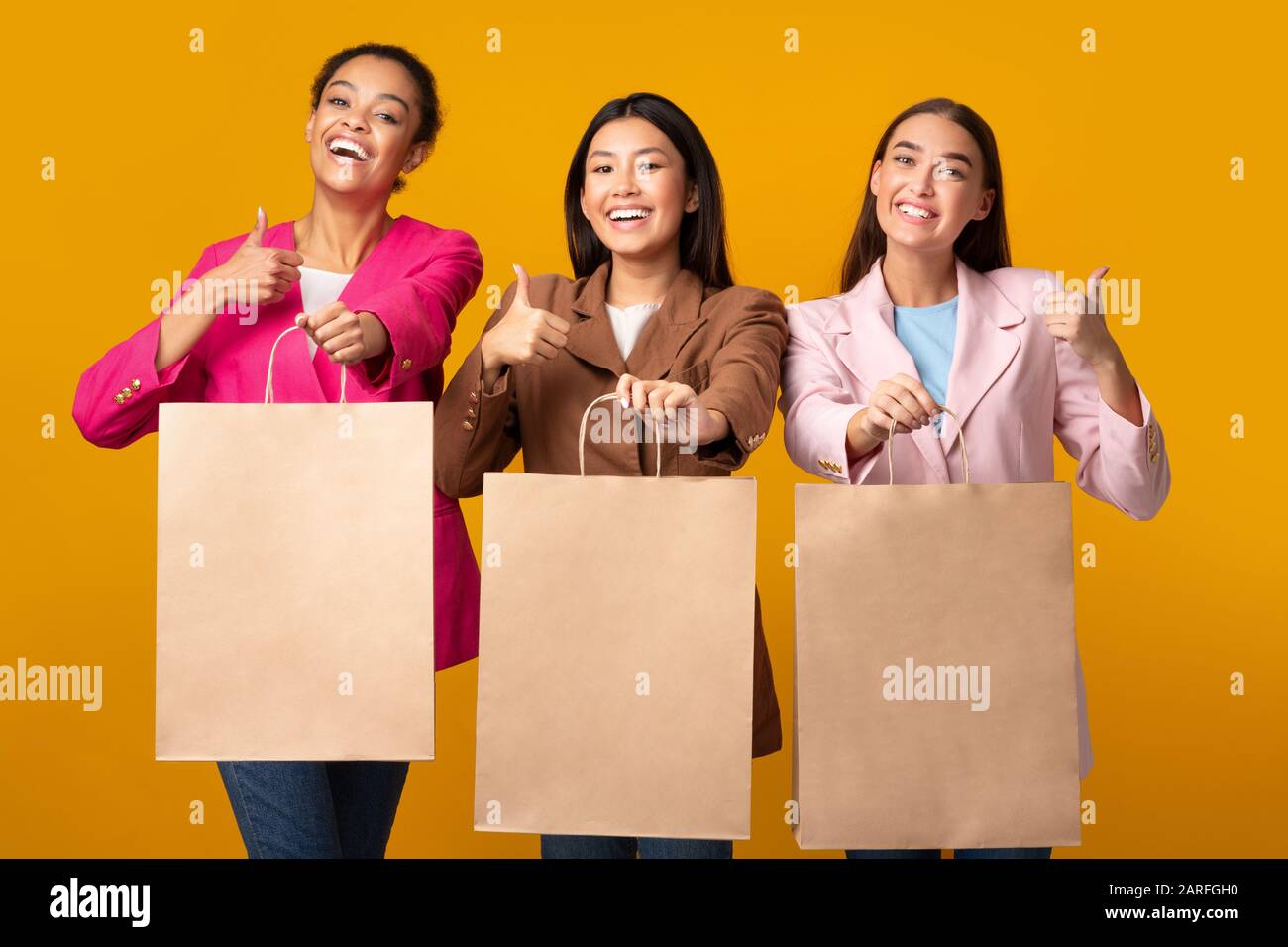 Three Girls Showing Shopper Bags Gesturing Thumbs-Up Posing In Studio Stock Photo