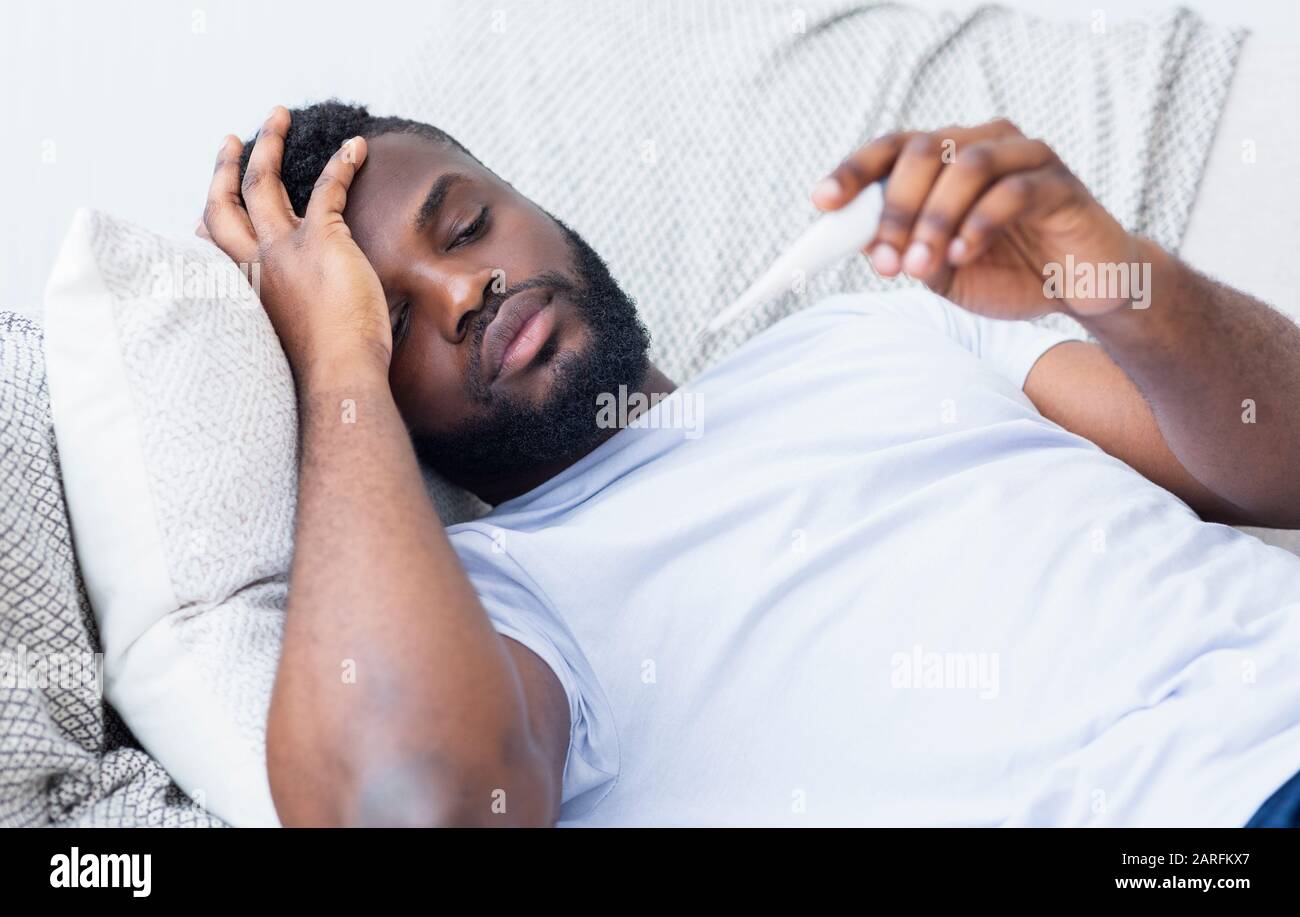 Sick african guy lying on sofa and checking his temperature Stock Photo