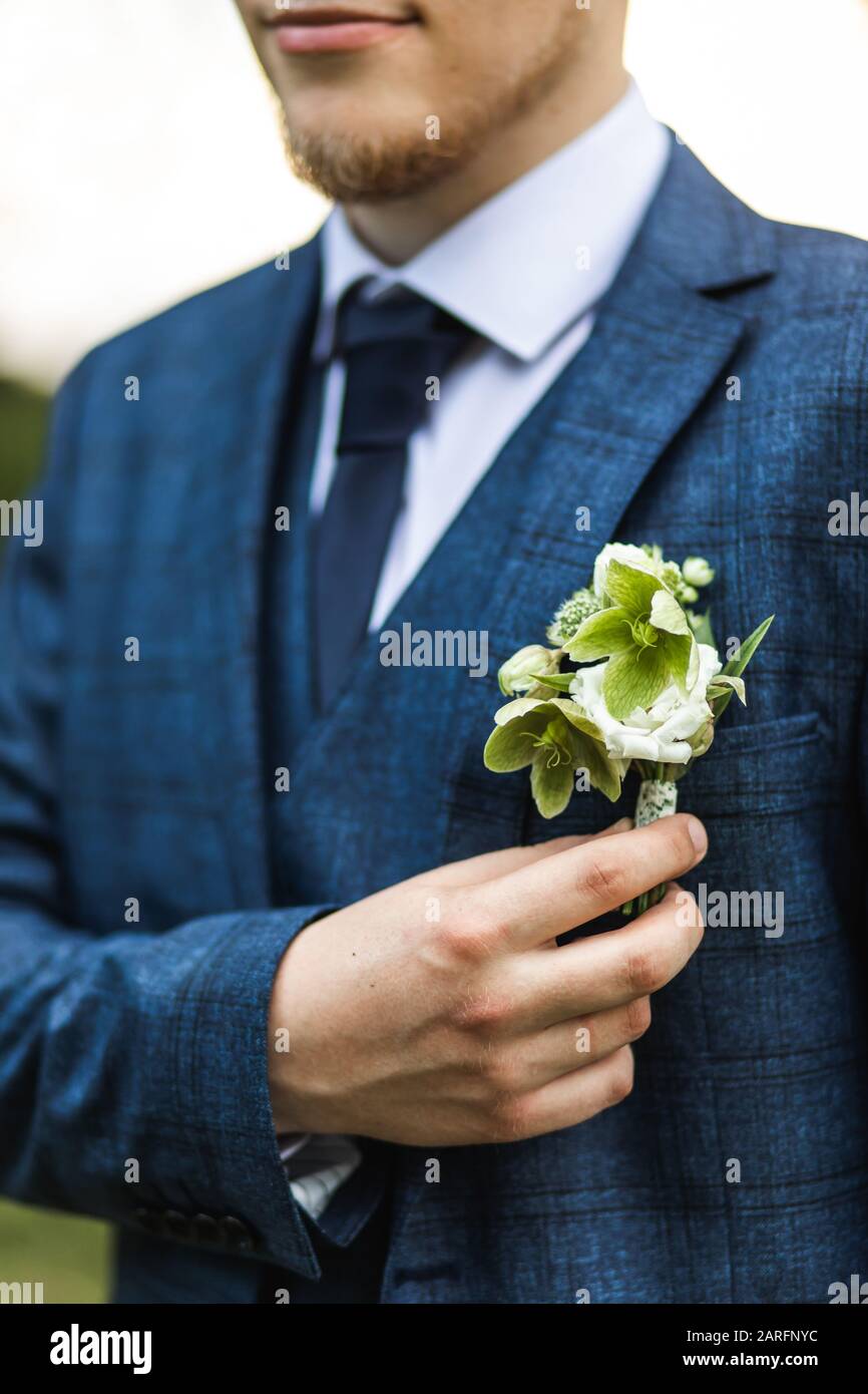 Stylish groom in classic blue suit holding green flower boutonniere. Rustic wedding style. Stock Photo