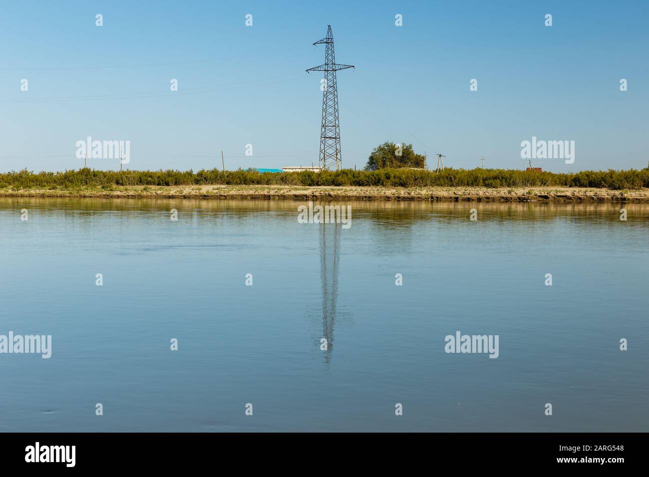 power line pylon stands on the banks of the Syr Darya river, reflected in the water, Kazakhstan. Power line crosses the river Stock Photo
