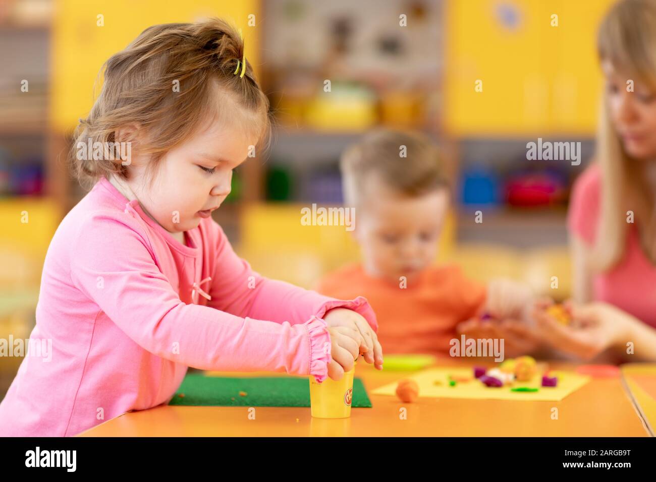 Kids girls with teacher play clay toys at day care center Stock Photo