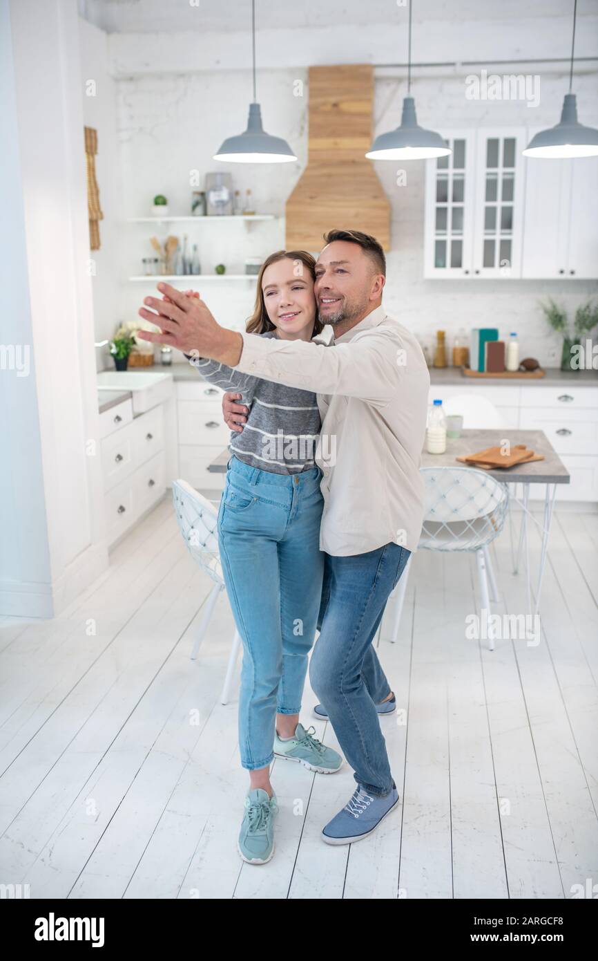 Dad and his teenage daughter are dancing in the kitchen. Stock Photo