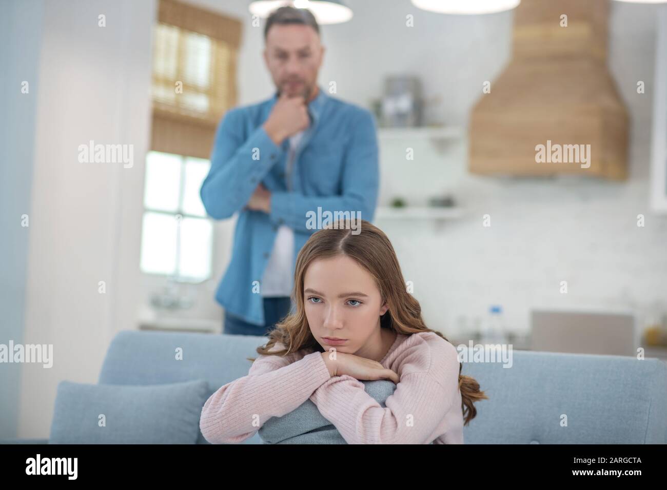 Pensive father standing behind seated sad daughter. Stock Photo