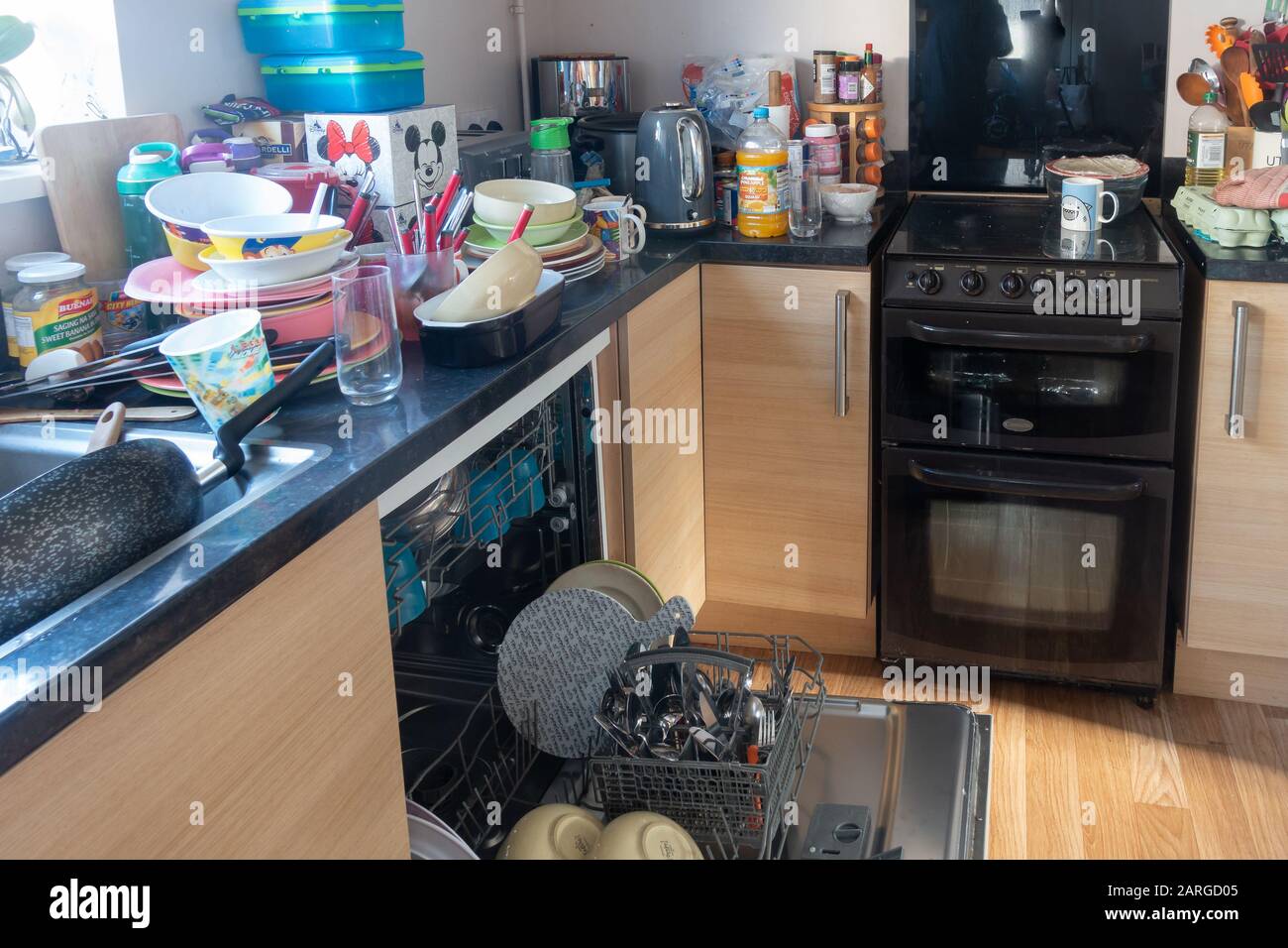 A dishwasher containing clean dishes with dirt dishes piled up by the side of the kitchen sink. Stock Photo