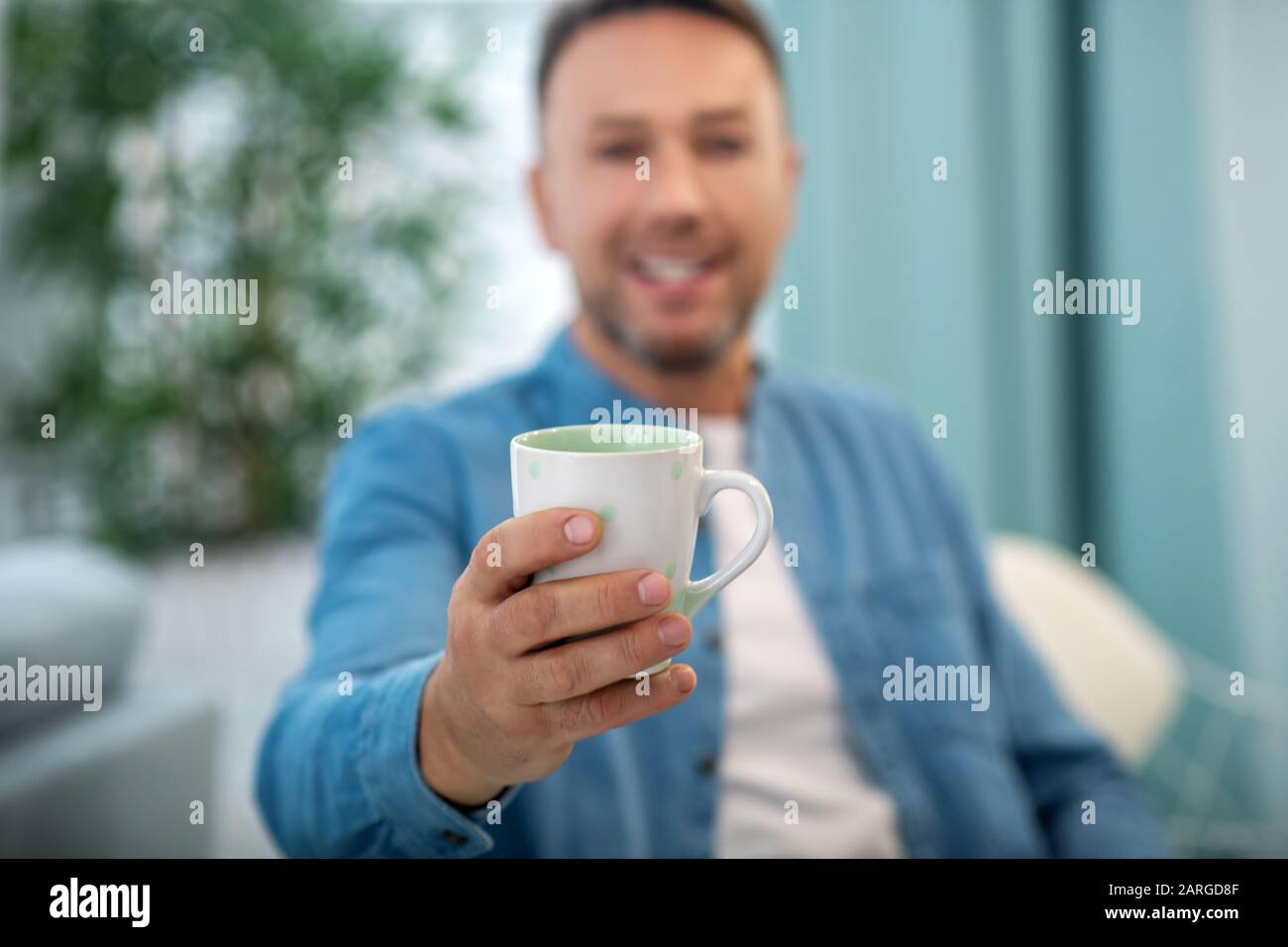 Cup of tea in the man's outstretched hand. Stock Photo