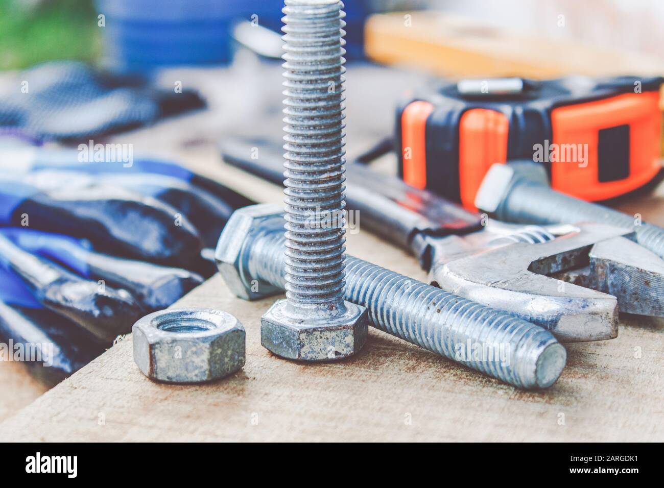 Steel bolt nuts and washers lie on wooden boards near an adjustable spanner and a tape measure