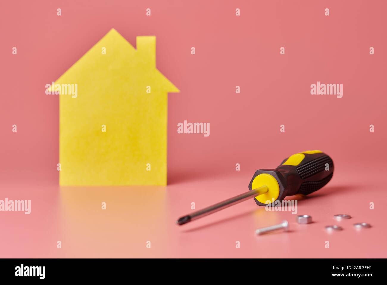 House renovation concept. Home repair and redecorated. Screws and yellow house shaped figure on pink background. Stock Photo