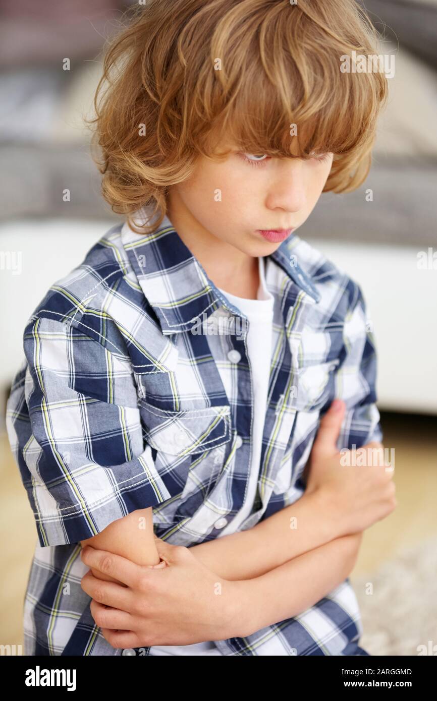 Child is defiant and stubborn at home with arms crossed and grimace Stock Photo