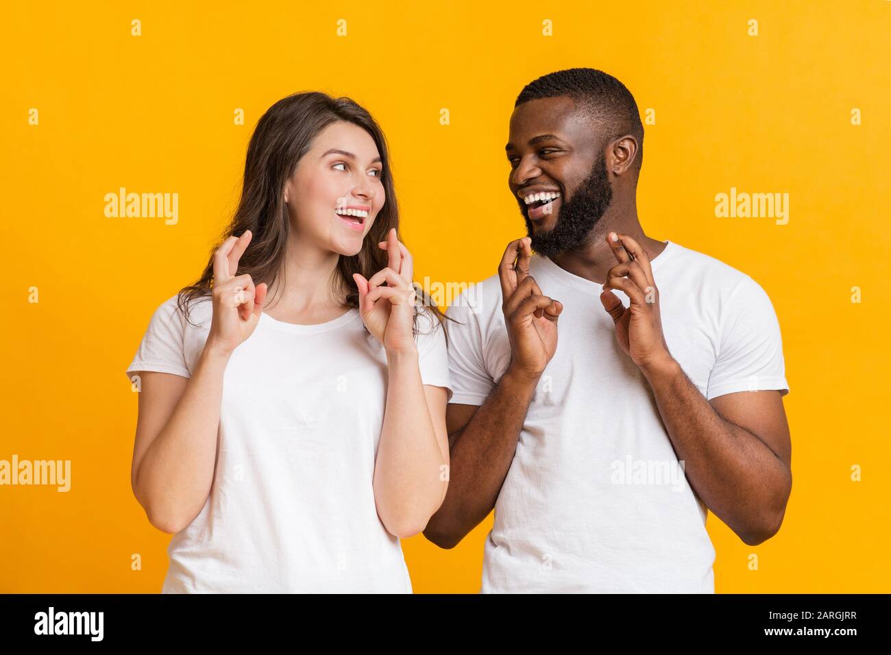 Cheerful interracial couple making wish, pleading for something with crossed fingers Stock Photo