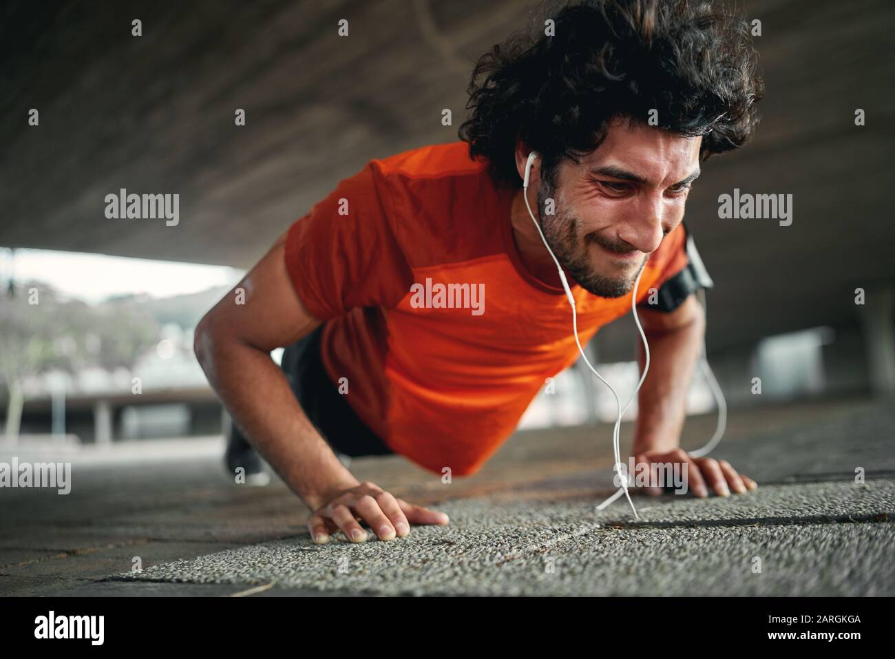 Young sportsman with earphones with painful face expression squeezed last push up - highly motivated and determined athlete  Stock Photo