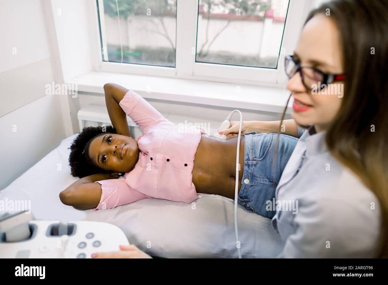 Young professional woman doctor doing an ultrasound of the kidneys of young African woman patient in modern medical clinic Stock Photo
