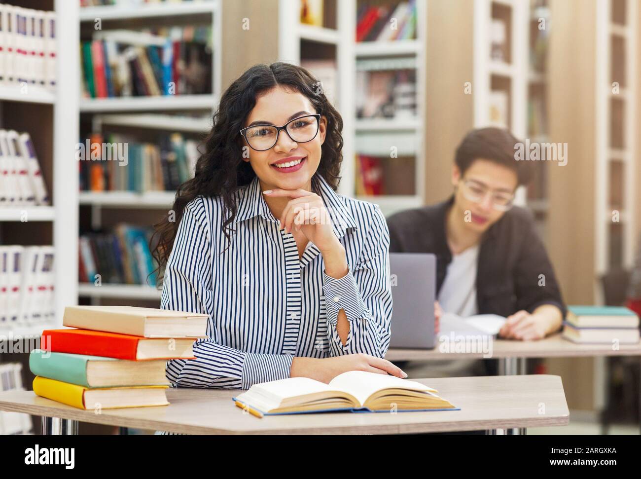 Cheerful latina girl sitting at desk in library Stock Photo