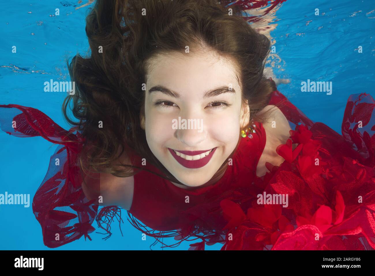 Portrait of young beautiful girl in a red dress posing underwater in the pool Stock Photo