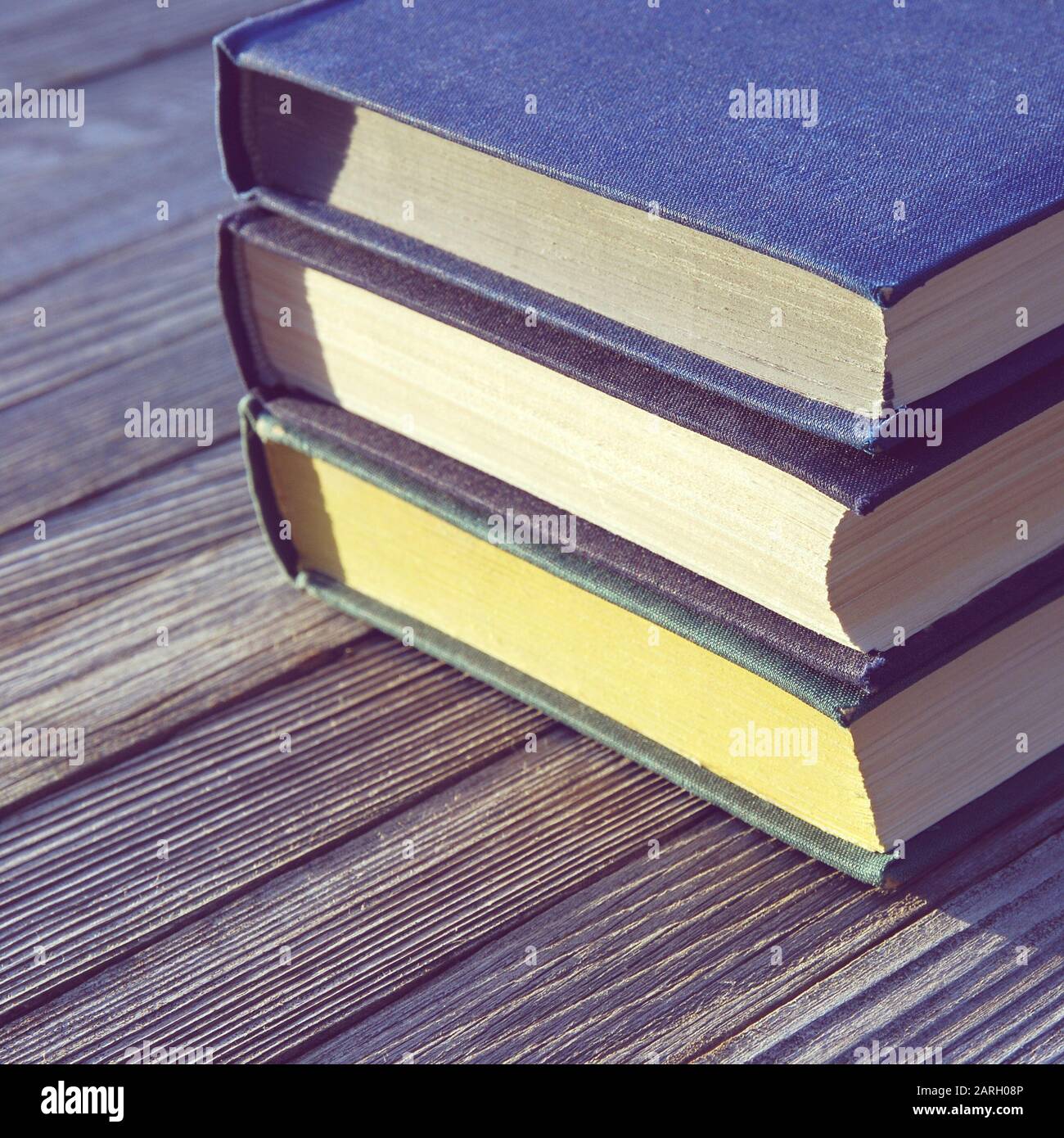 Three old books stacked in a pile on old wooden table, square frame Stock Photo