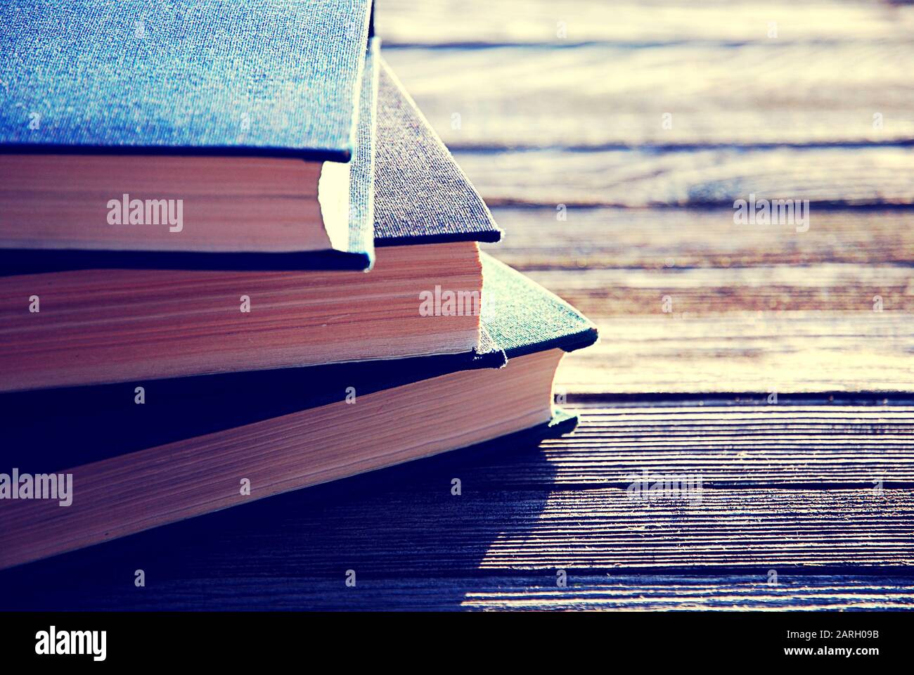 Stack of three old books in backlight on wooden table, selective focus Stock Photo