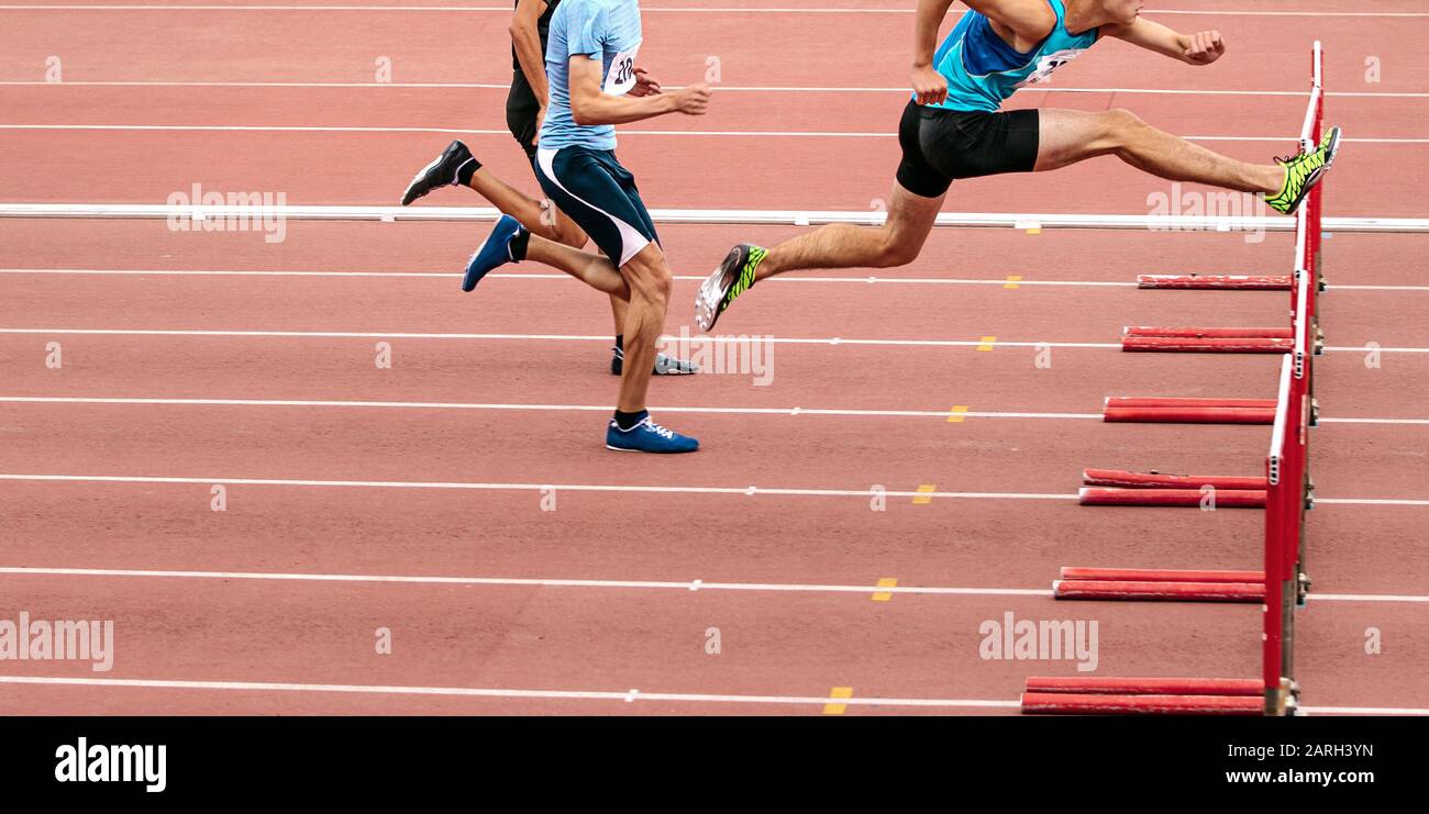 race men athletes run 110 meters hurdles in athletics competition Stock