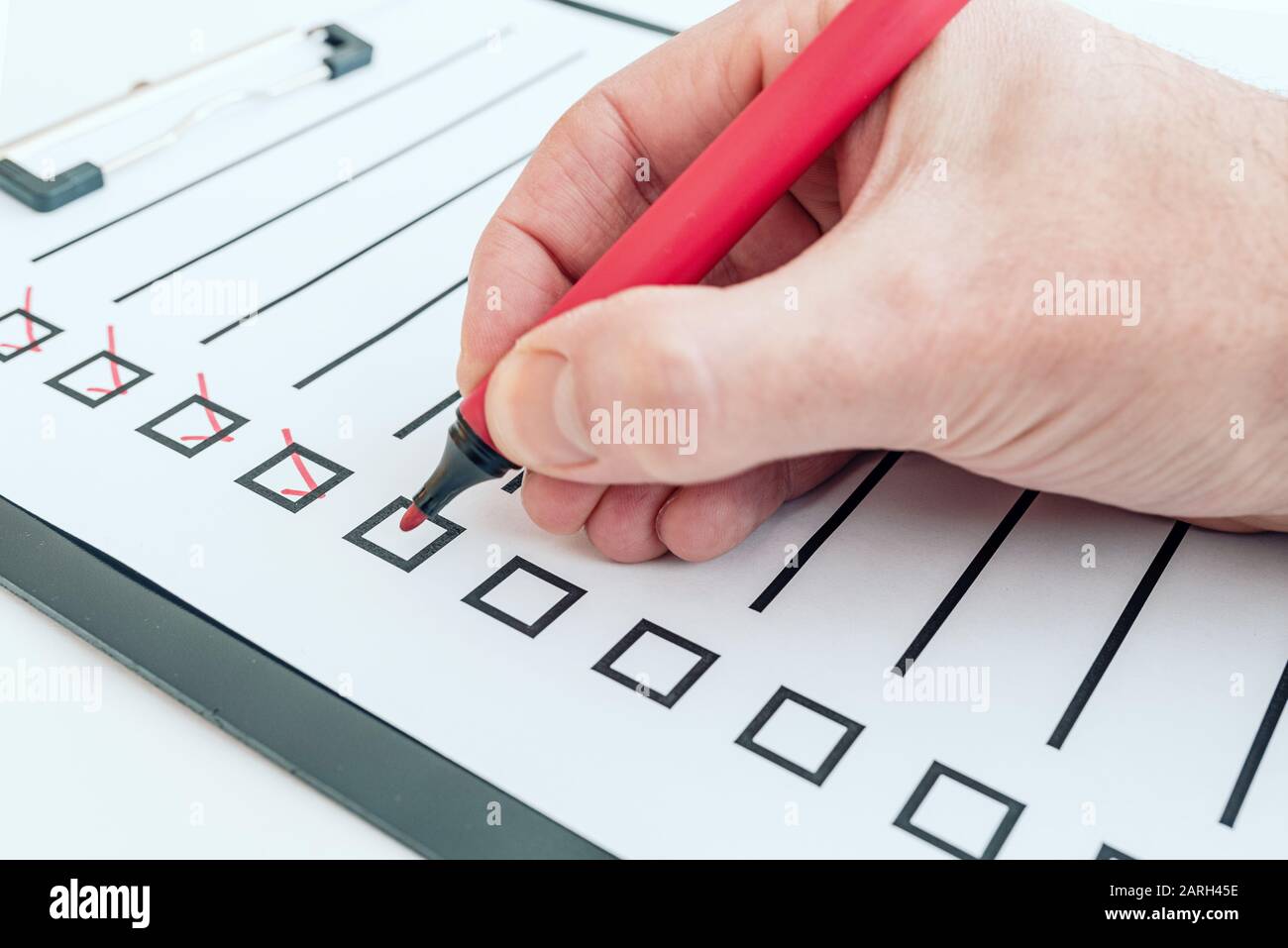closeup of hand holding red pen ticking off checklist or todo list on