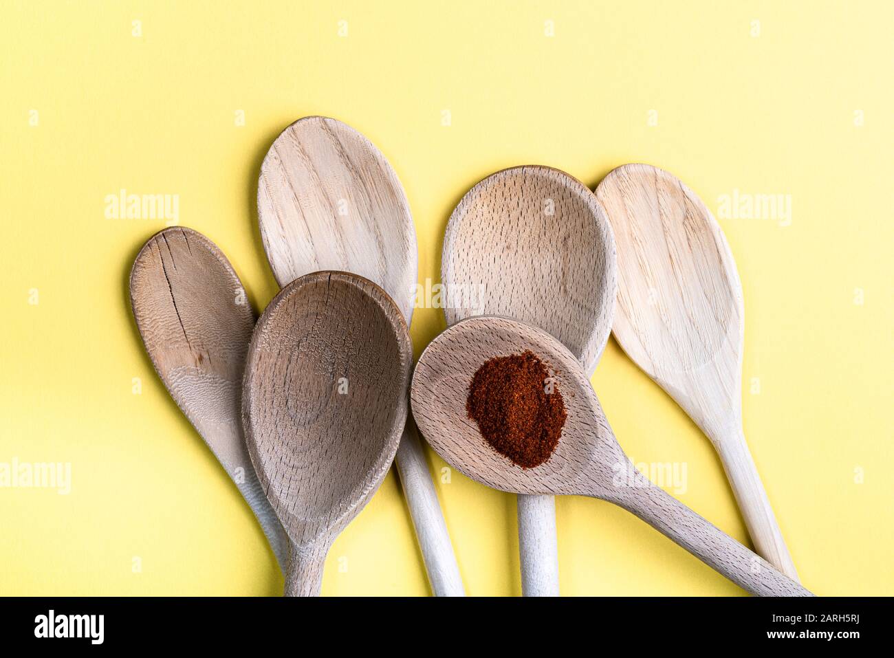 Group of old wooden spoons isolated on a pale cream background. One with some paprika. Stock Photo